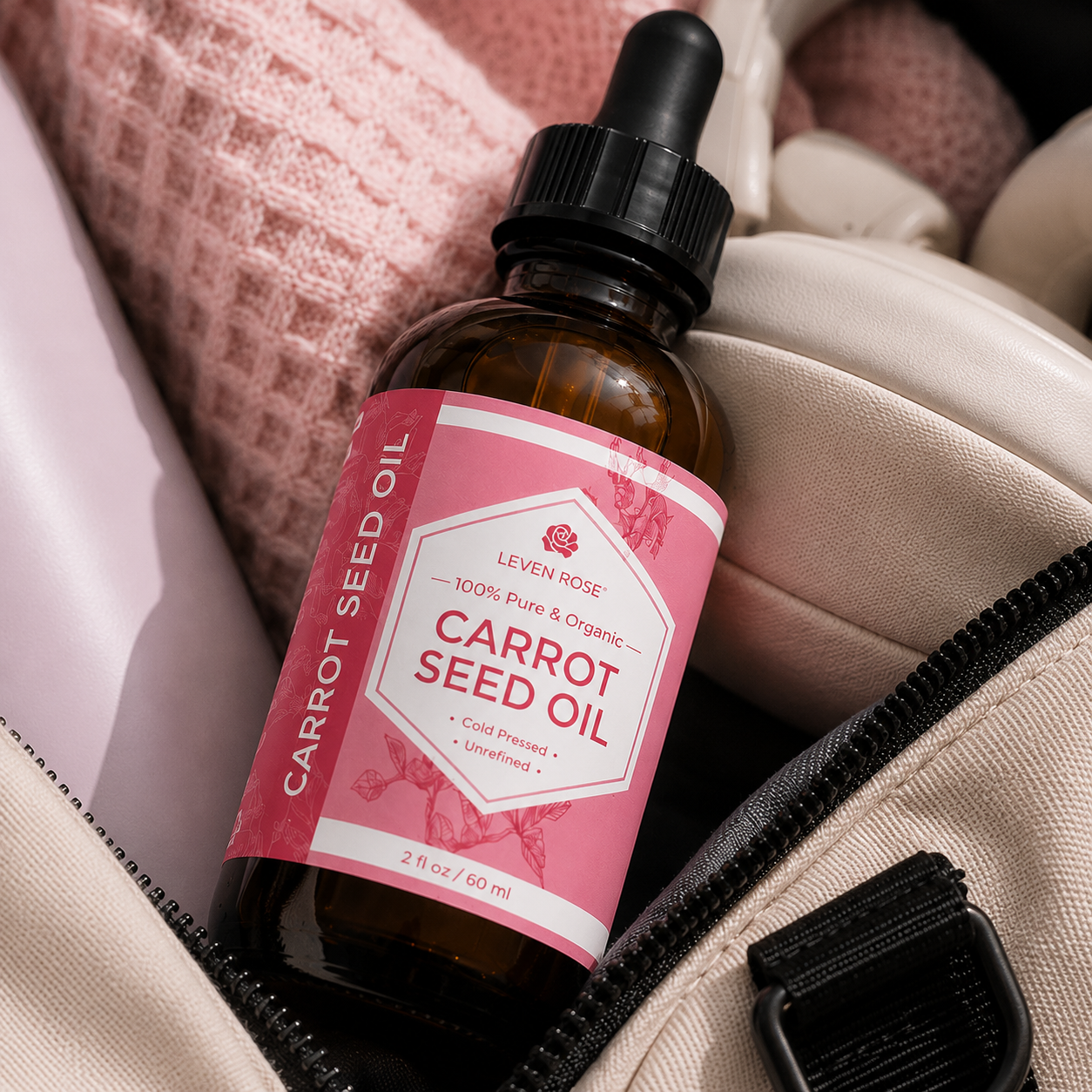 A bottle of Leven Rose Carrot Seed Oil resting inside a beige zippered pouch with a pink knit fabric in the background.