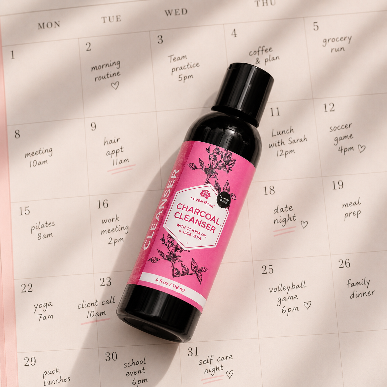 A bottle of Jane's Charcoal Cleanser resting diagonally on a printed monthly planner calendar page.