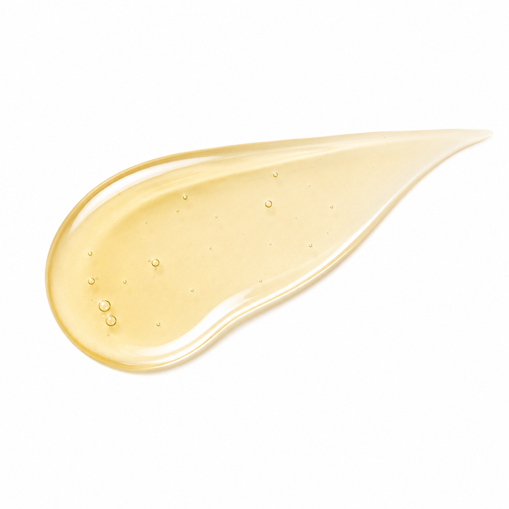 A teardrop-shaped smear of translucent golden-yellow cosmetic cream or serum on a solid white background, showing small embedded air bubbles.