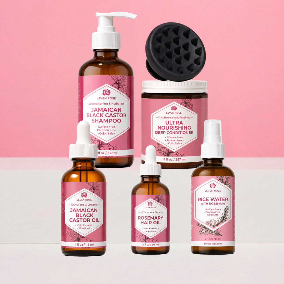 A set of six haircare products from Levain Rose arranged on a two-tone pink and white background. The products include a Jamaican Black Castor Shampoo in an amber bottle with a pump, an Ultra Nourishing Deep Conditioner in a jar with a black applicator on top, a Jamaican Black Castor Oil dropper bottle, a Rosemary Hair Oil dropper bottle, and a Rice Water with Rosemary spray bottle.