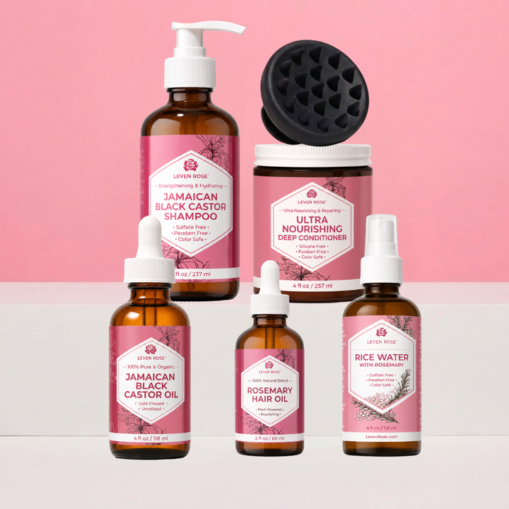 A set of six haircare products from Levain Rose arranged on a two-tone pink and white background. The products include a Jamaican Black Castor Shampoo in an amber bottle with a pump, an Ultra Nourishing Deep Conditioner in a jar with a black applicator on top, a Jamaican Black Castor Oil dropper bottle, a Rosemary Hair Oil dropper bottle, and a Rice Water with Rosemary spray bottle.