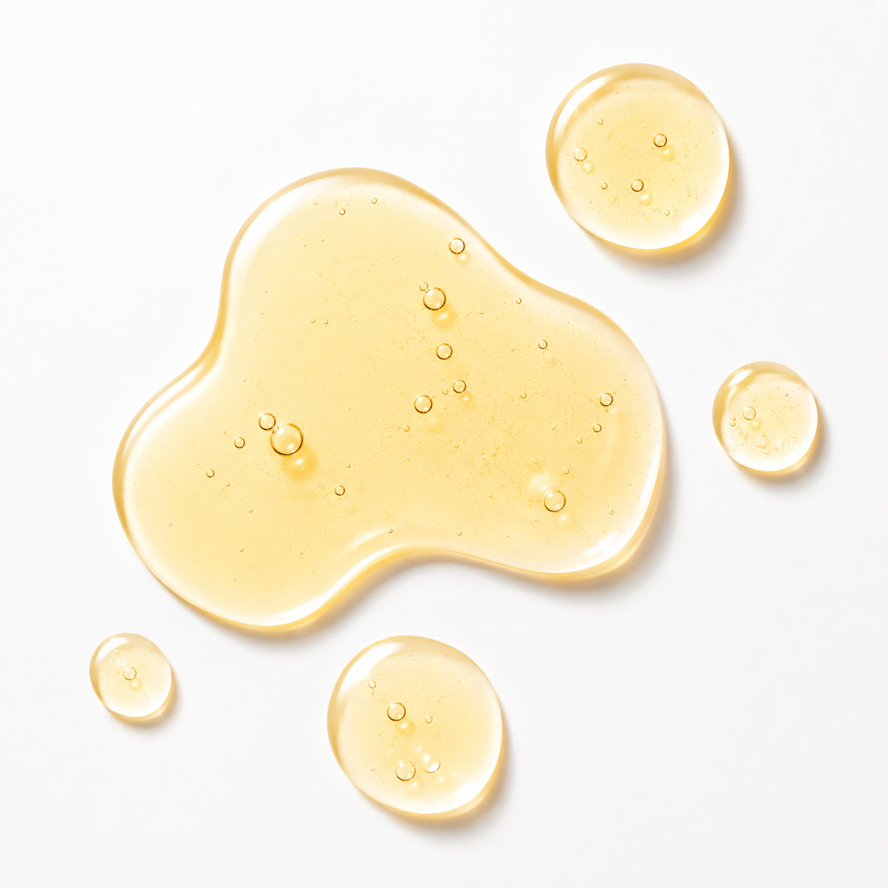 A glossy, translucent golden-yellow liquid cosmetic or skincare droplet with small air bubbles, arranged on a clean white background.