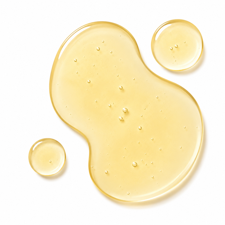 A translucent golden-yellow liquid cosmetic or oil spread in an irregular blob shape with two smaller droplets on a clean white background.