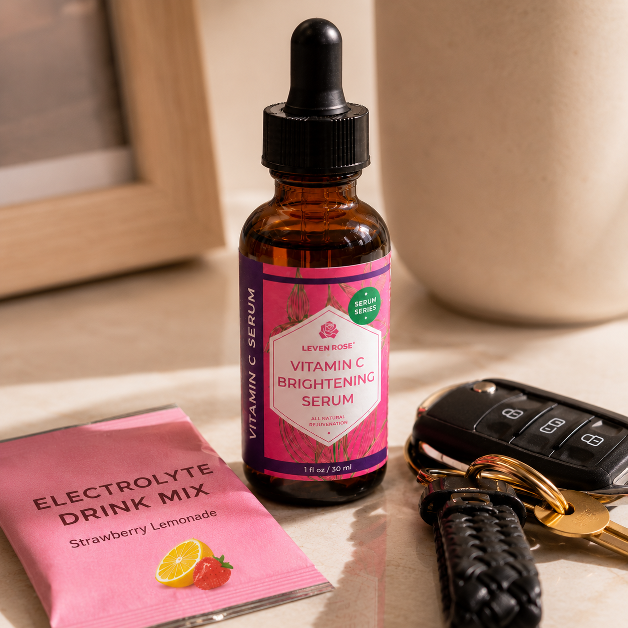 A bottle of LevenRose Vitamin C Brightening Serum with a pink label and dropper cap, shown on a tabletop next to an Electrolyte Drink Mix packet, car keys, and a beige ceramic mug.