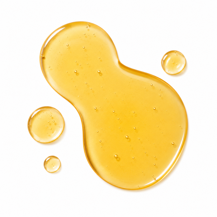 A glossy, translucent golden-yellow liquid spread in an irregular blob shape with three smaller droplets on a solid white background.