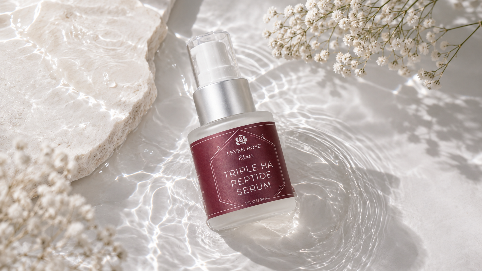 A bottle of Leaky Rose Clink Triple HA Peptide Serum is displayed in a styled flat-lay setting with water ripples, a white stone slab, and baby's breath flowers.