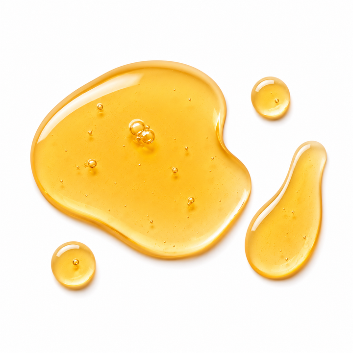 Golden translucent honey-like substance spread in irregular pools with a few small droplets on a clean white background.