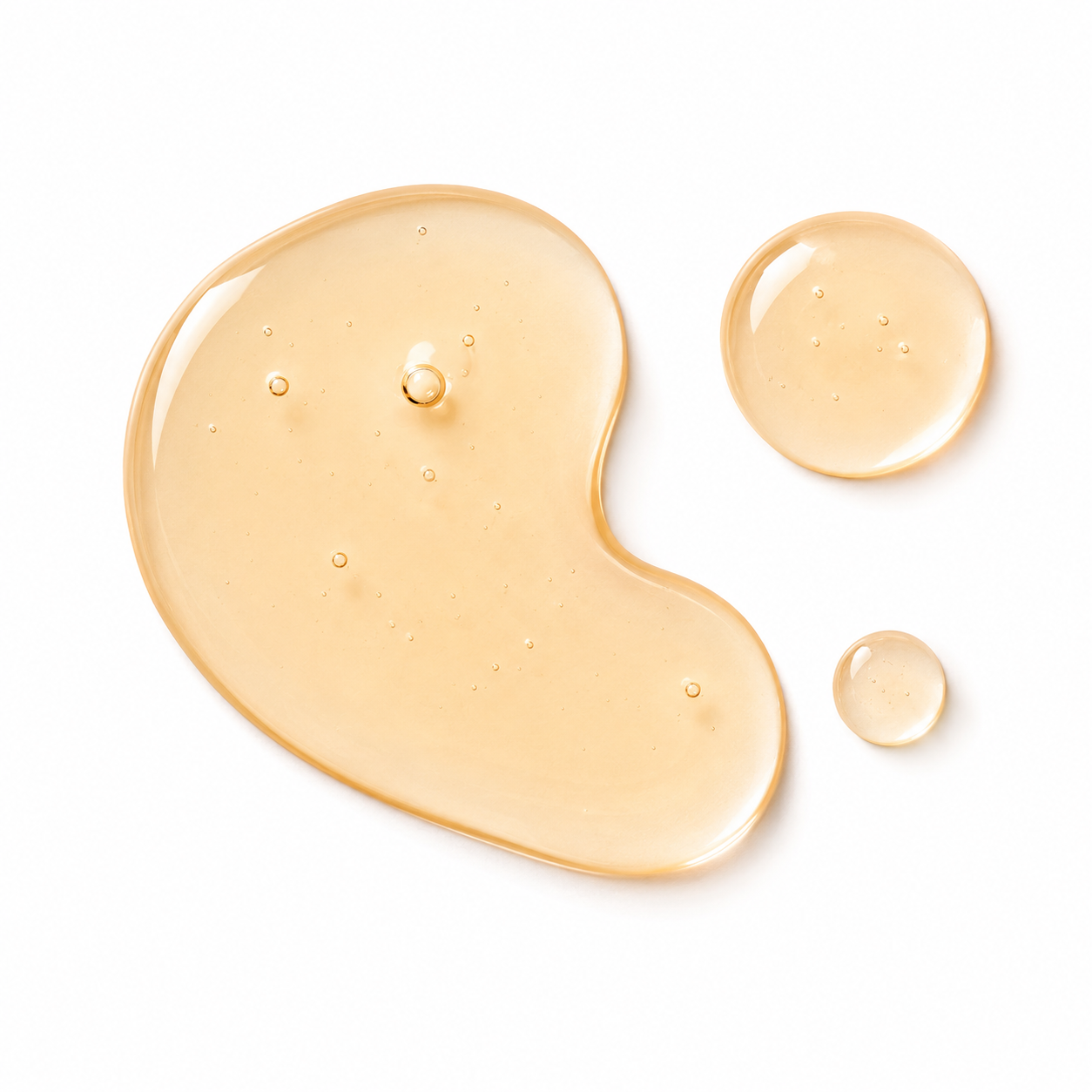 Three translucent droplets of golden-beige cosmetic gel or serum on a clean white background, including one larger irregular puddle and two smaller round drops.